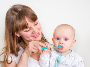 Lavare i denti ai bambini: una bambina si spazzola i denti assistita dalla mamma