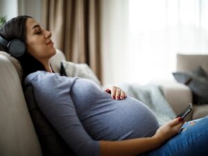 gravidanza e accortezze: una mamma seduta sul divano con gli occhi chiusi ascolta la musica e si tiene la pancia